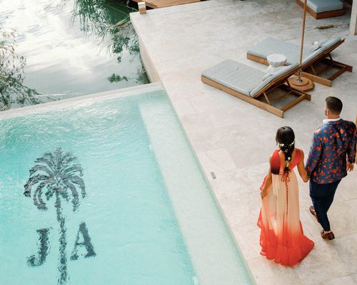 bride and groom in colorful attire walking next to pool with monogram