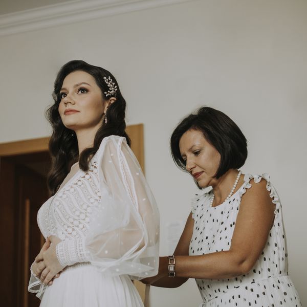 mother of the bride in white polka dot dress zipping up bride in bohemian wedding dress