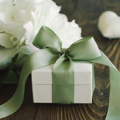 White gift box with green ribbon next to white peonies