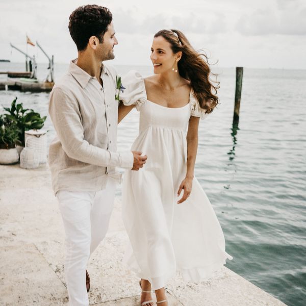 bride wearing an empire waist wedding dress walking with groom by the sea