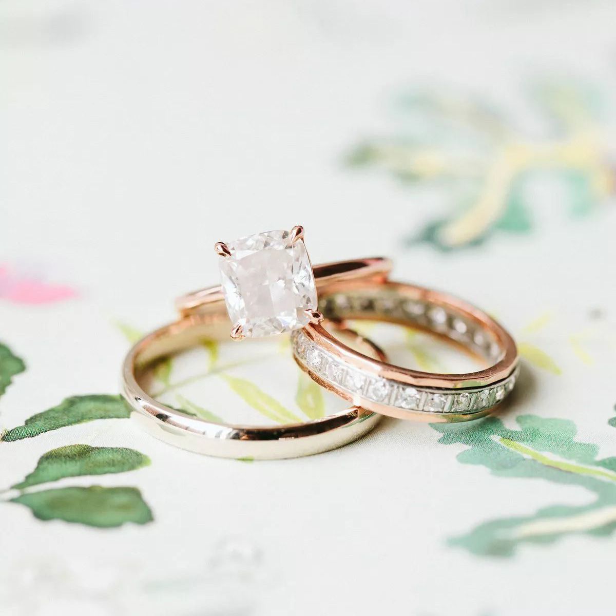 Cushion-cut engagement ring on rose gold band beside two wedding bands