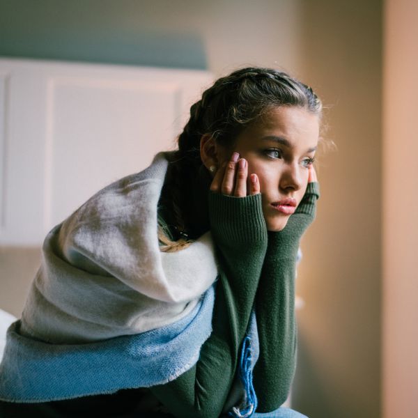 Young woman sitting at the bed and looking through the window