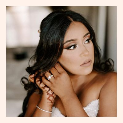 A bride putting on her earrings and showcasing her diamond engagement ring 