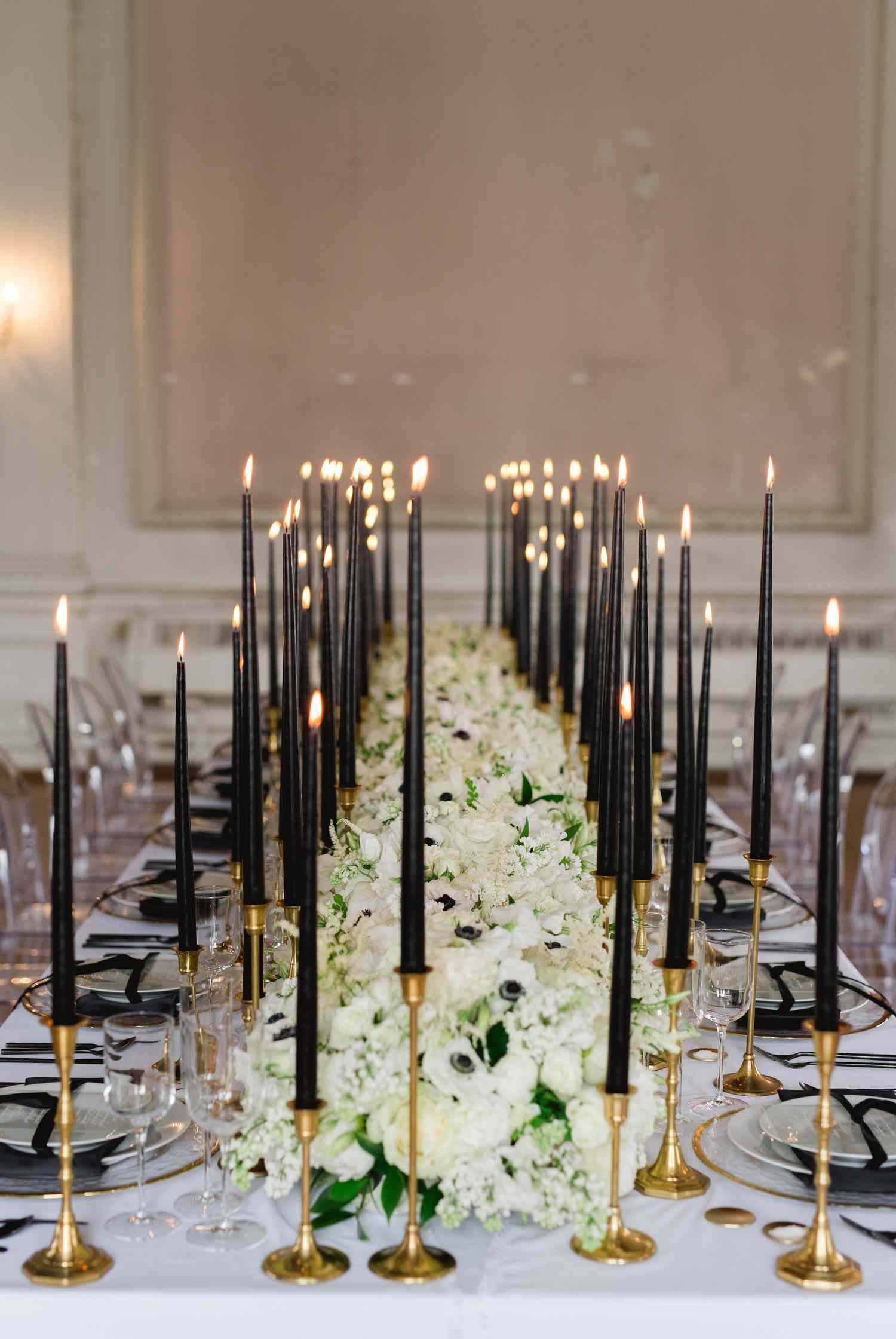 Tall black taper candles with gold holders on table with white floral arrangements