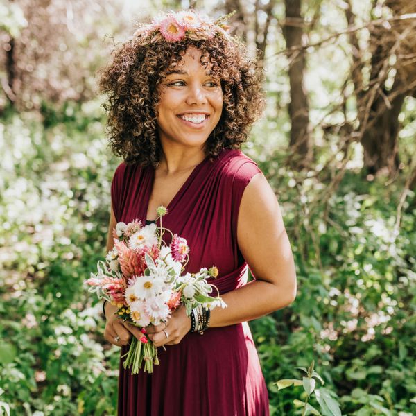 Woman standing in woods with fresh flowers, a burgundy dress, and floral crown