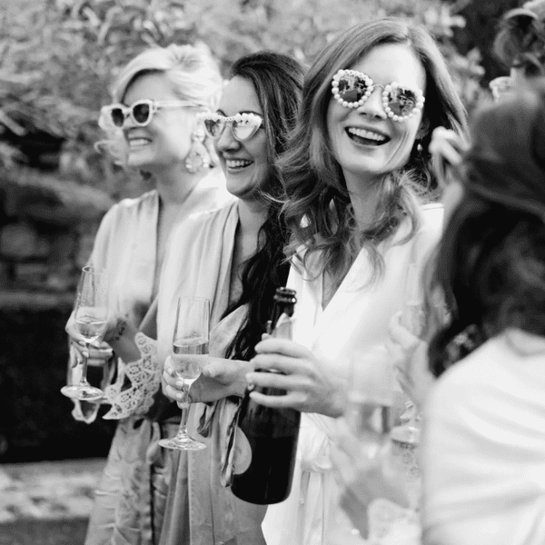 Bide and bridesmaids in sunglasses holding champagne and smiling