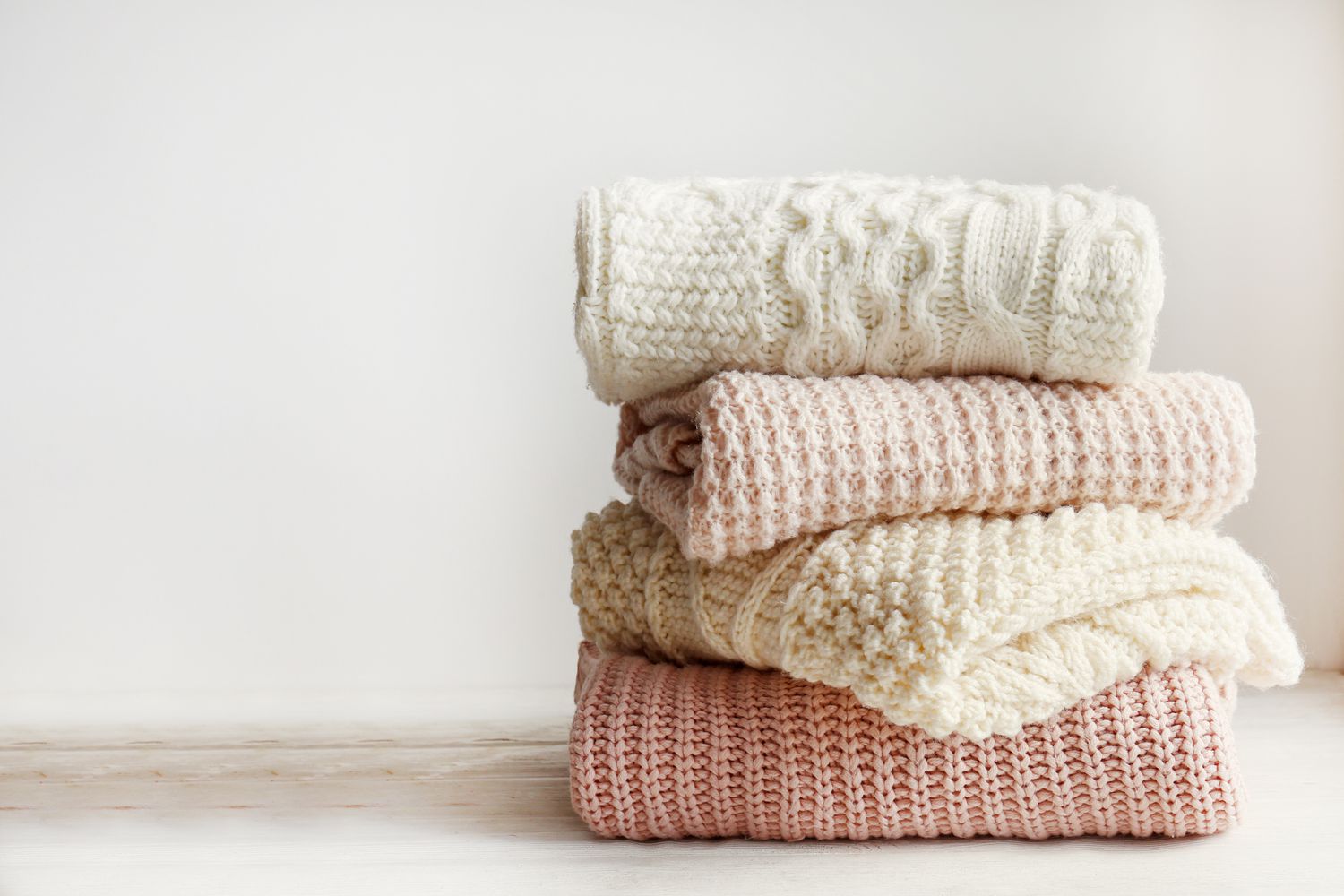 A pile of folded wool cable-knit sweaters in cream and peach tones