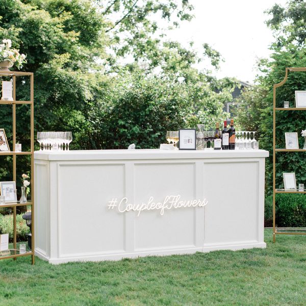 An white bar outside decorated with a neon sign displaying the couple's hashtag