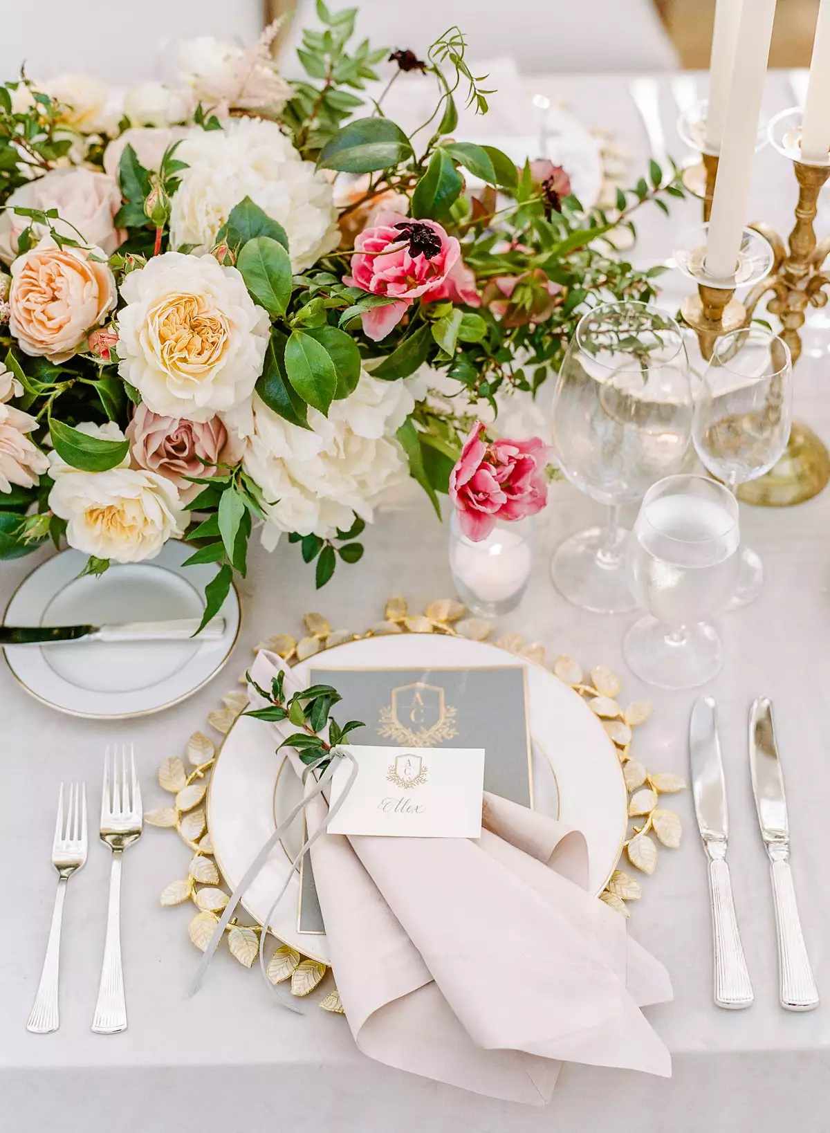 Place setting with gold leaf charger, pink napkin, gray menu, and pink and white floral arrangements