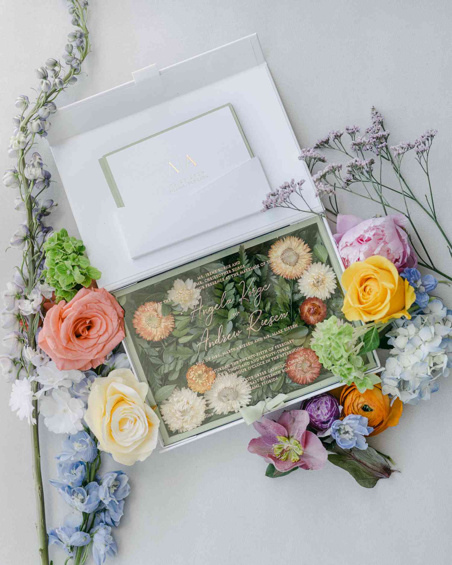 A floral-themed boxed wedding invitation with fresh flowers.