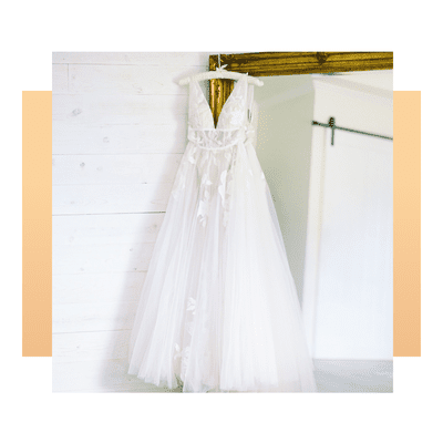 White a-line wedding dress with plunging neckline and floral embroidery hanging on silk hanger in front of mirror