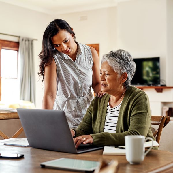 young woman helping her grandmother with her finances on a laptop in their home