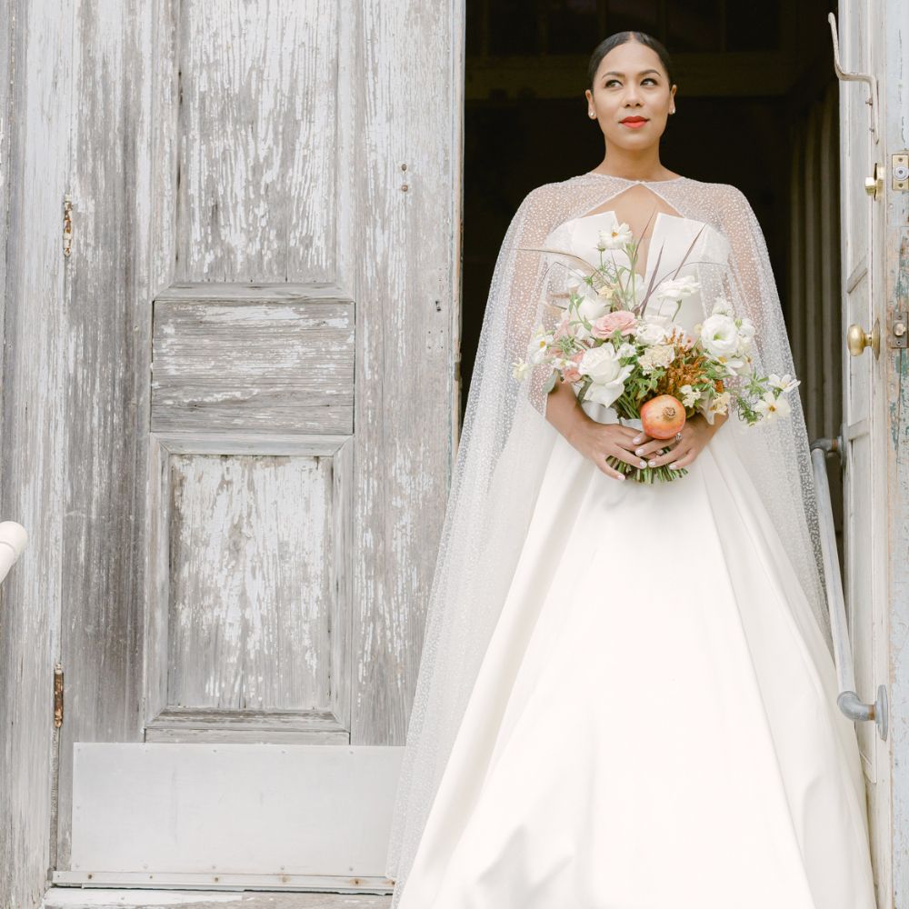 bride posing in front of an open church door wearing a strapless wedding dress with a sequin cape