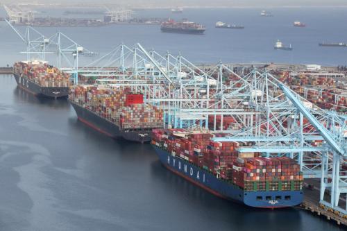 Ships stacked with containers docked at a port, with cranes moving containers