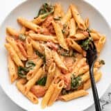 Overhead view of a bowl full of creamy tomato and spinach pasta, a black fork in the side