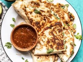 Close up of a plate full of creamy white bean and spinach quesadillas with a dish of red salsa