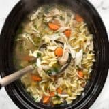 Overhead view of a ladle lifting chicken noodle soup out of the slow cooker