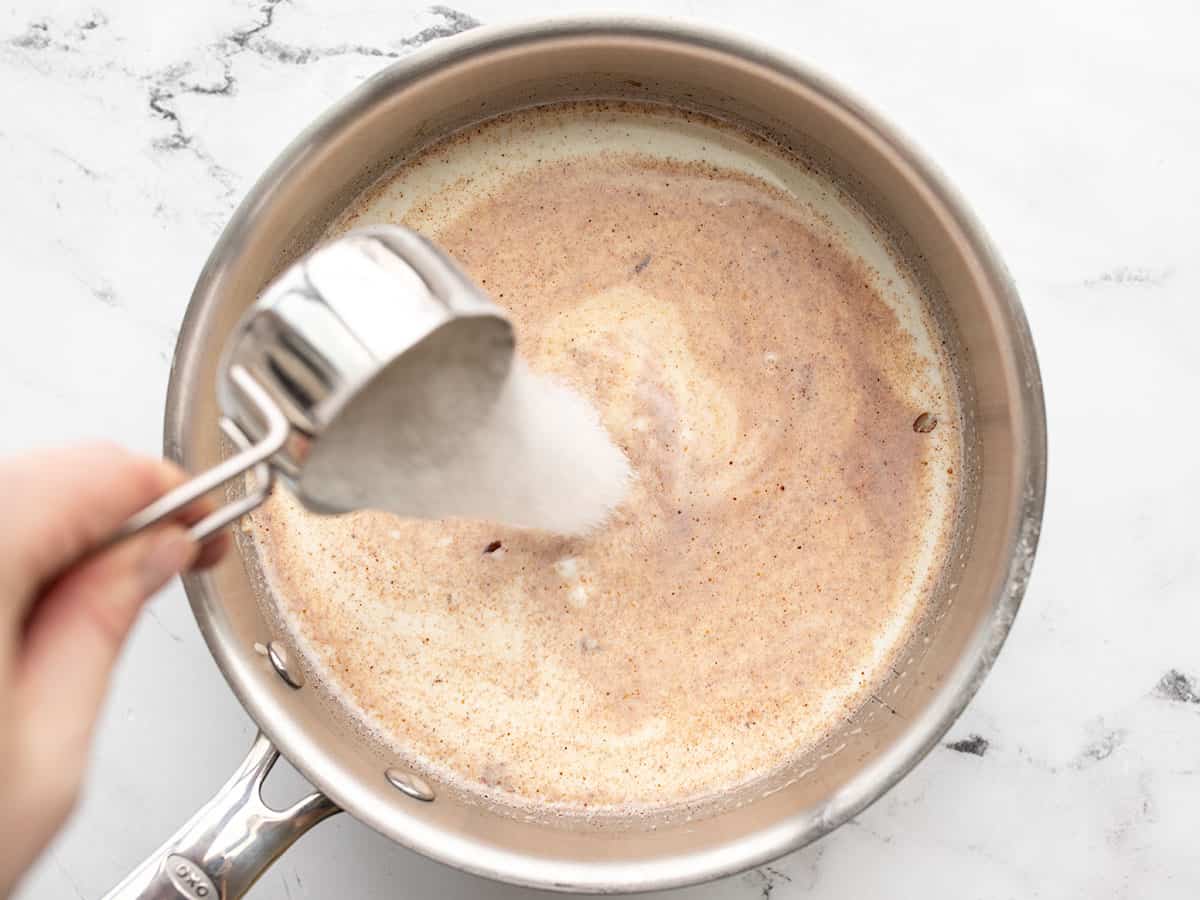 sugar being poured into the pot with the milk and rice.