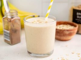 Side view of a glass full of peanut butter banana smoothie with a yellow striped straw.