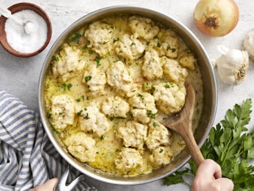 Chicken and dumplings in the skillet being scooped out with a spoon.