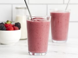 Front view of two mixed berry smoothies in a glass with a metal straw.