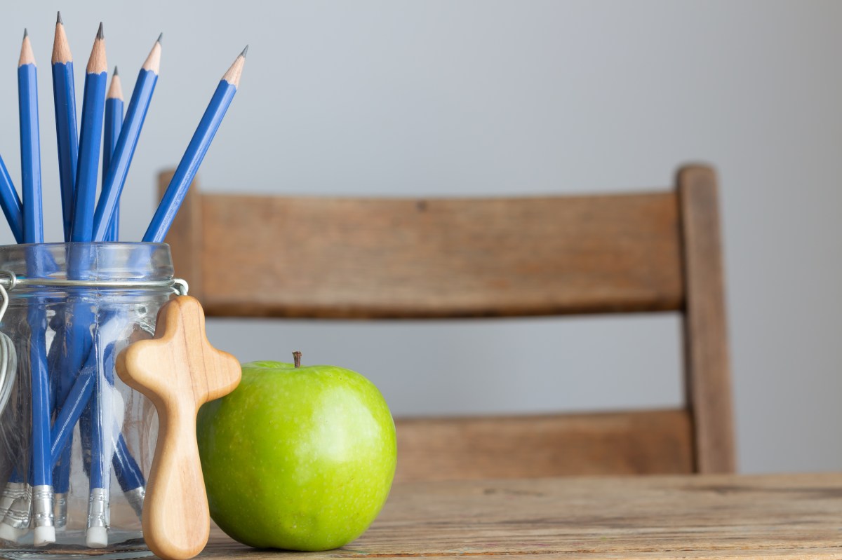 cross, green apple and pencils on desk with white background