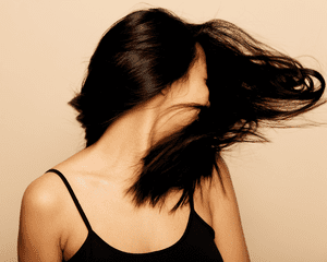 A woman with dark shiny hair splayed in front of her face as she turns her head