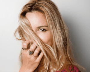 A blonde woman holding her hair in front of half of her face