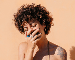 A woman with tattoos on her shoulder, hand and finger, covering her mouth with her hand as she laughs