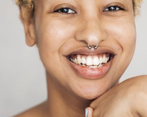 Smiling person with short, blonde curls and septum piercing