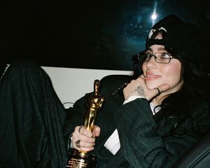 Billie Eilish poses in pinstriped suit with her Oscar trophy while showing off her fairy hand tattoo