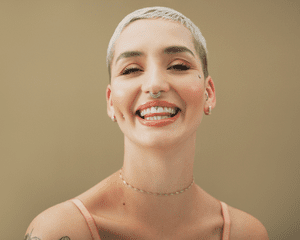 Close up of a woman with a blonde buzz cut and lip and nose piercings.