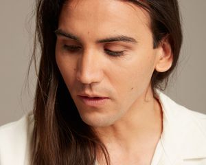 Young man with long hair wearing a clean minimal outfit in a studio shoot over grey background