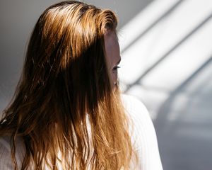 Woman with auburn hair over her eye, standing in shadows