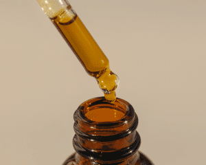 close up of golden oil dropper on tan background