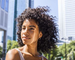 woman with curly hair looking content in front of building