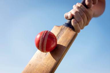 Cricket player batsman hitting a ball with a bat shot from below against a blue sky