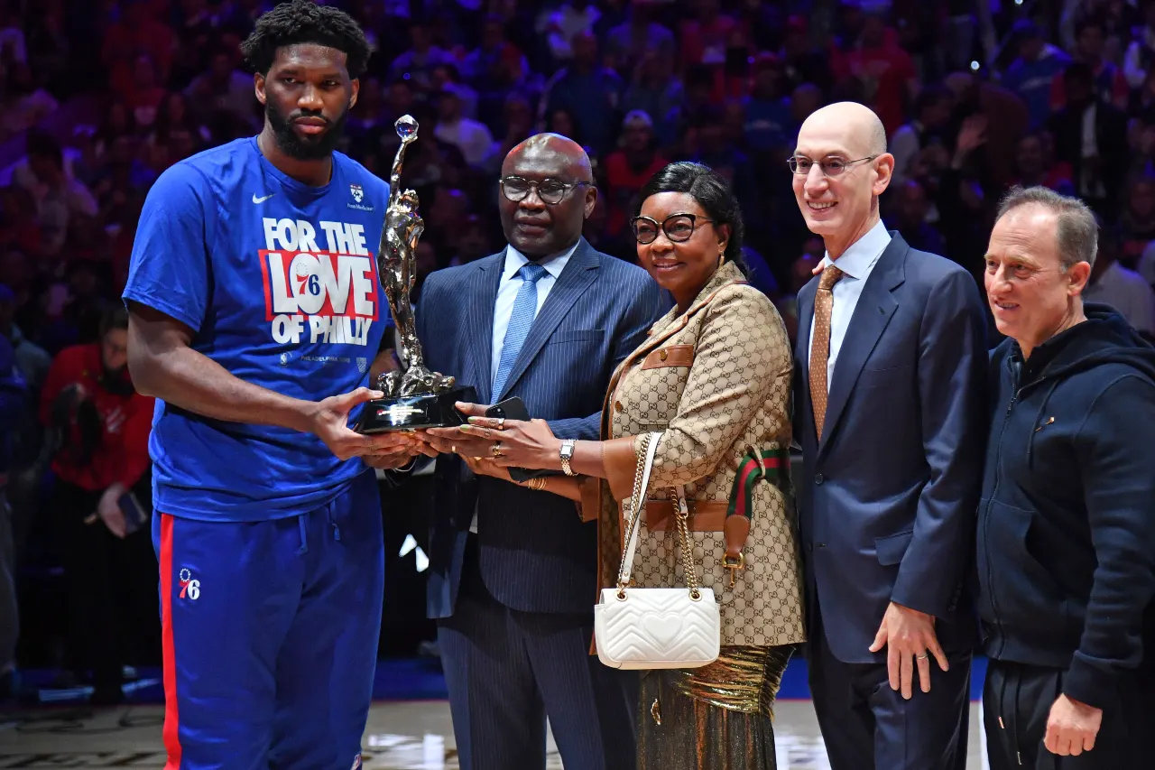 Philadelphia 76ers center Joel Embiid (21) holds the MVP trophy with his parents Thomas and Christine, along with NBA Commissioner Adam Silver and 76ers owners Josh Harris before game three of the 2023 NBA playoffs against the Boston Celtics at Wells Fargo Center.