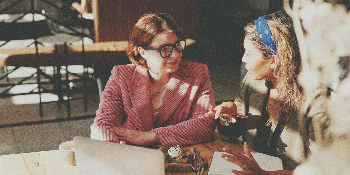 Woman in pink sitting at a table talking to woman with blonde hair