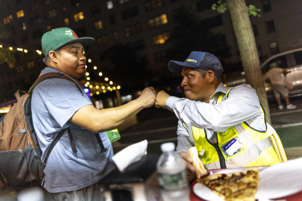 Sergio Solano, an immigrant from Mexico, right, greets his friend at a pizza shop at the end of his work day, June 21, 2024, in New York.