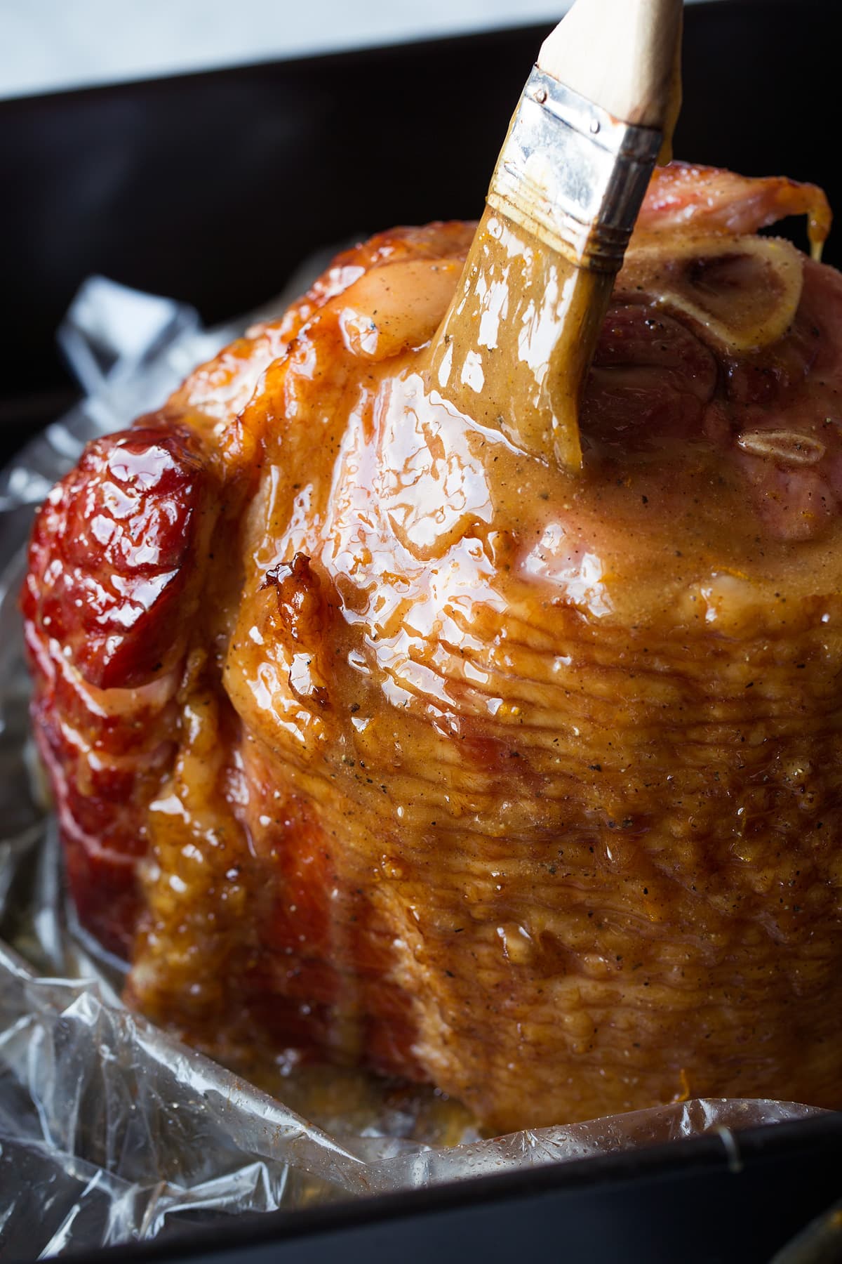 Brushing glaze over honey baked ham in roasting pan