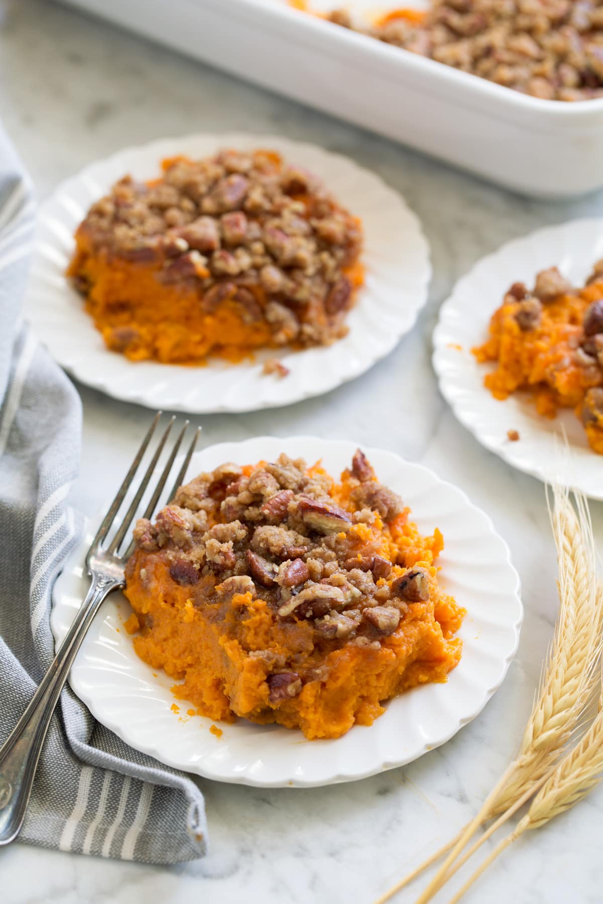 Sweet Potato Casserole shown in three individual servings and small white scalloped plates set over a marble surface.