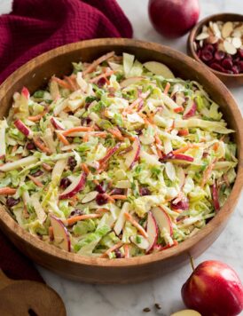 Homemade apple slaw with shredded cabbage, apples, carrots, almonds and dressing shown in a wooden salad bowl.