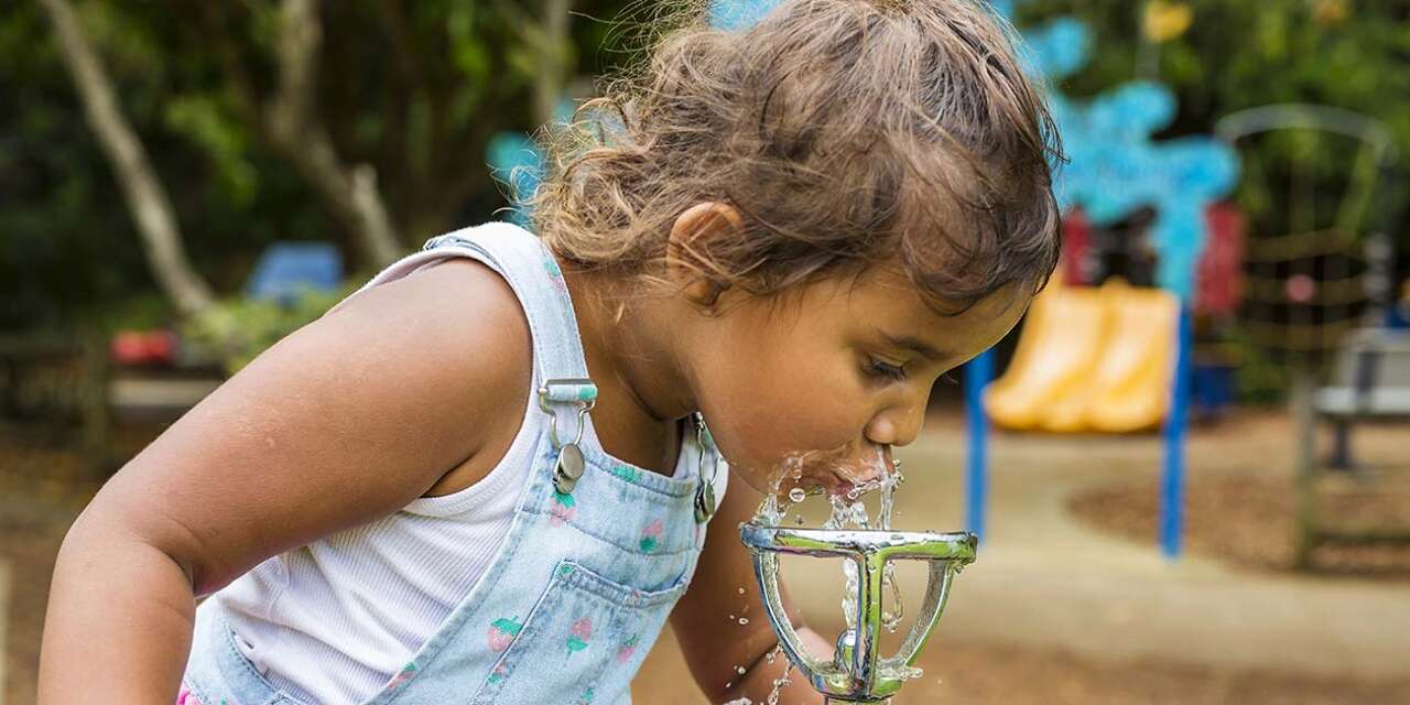 Little girl drinking from water fountain at a park