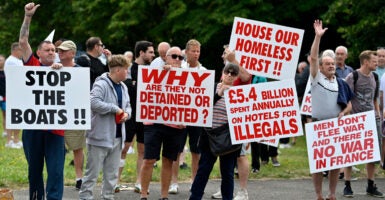 Several British men on a roadside protesting illegal aliens with large signs that say things such as "stop the boats"