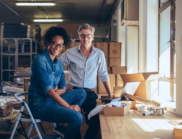 Peninsula Group Limited - An employer and their employee smiling at the camera while in a cluttered workspace