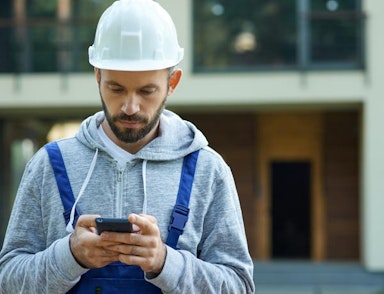 Peninsula Group Limited - An employer wearing a hard hat updates his Brightsafe software on his phone