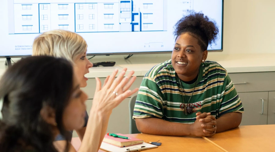 Three women sit at a conference table.