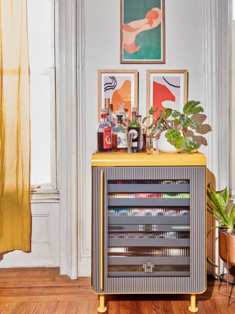 Yellow Rocco beverage fridge with bottles and a plant on top