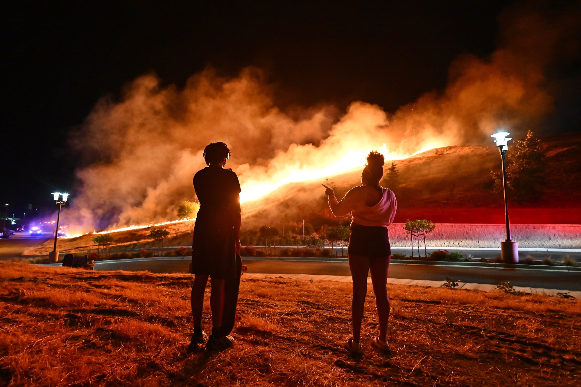 Caden Pollard, 16, from left, and his sister Mia Pollard, 17, watch as a vegetation fire caused by illegal fireworks endangers homes on Lotus Court during the Fourth of July celebrations in Antioch, Calif., on Thursday, July 4, 2024. (Jose Carlos Fajardo/Bay Area News Group)